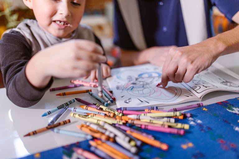 A child and adult share a creative coloring session with crayons on a table.
