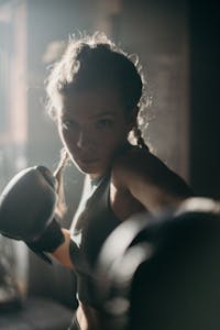 Focused female boxer in action, throwing a punch in a dimly lit gym.