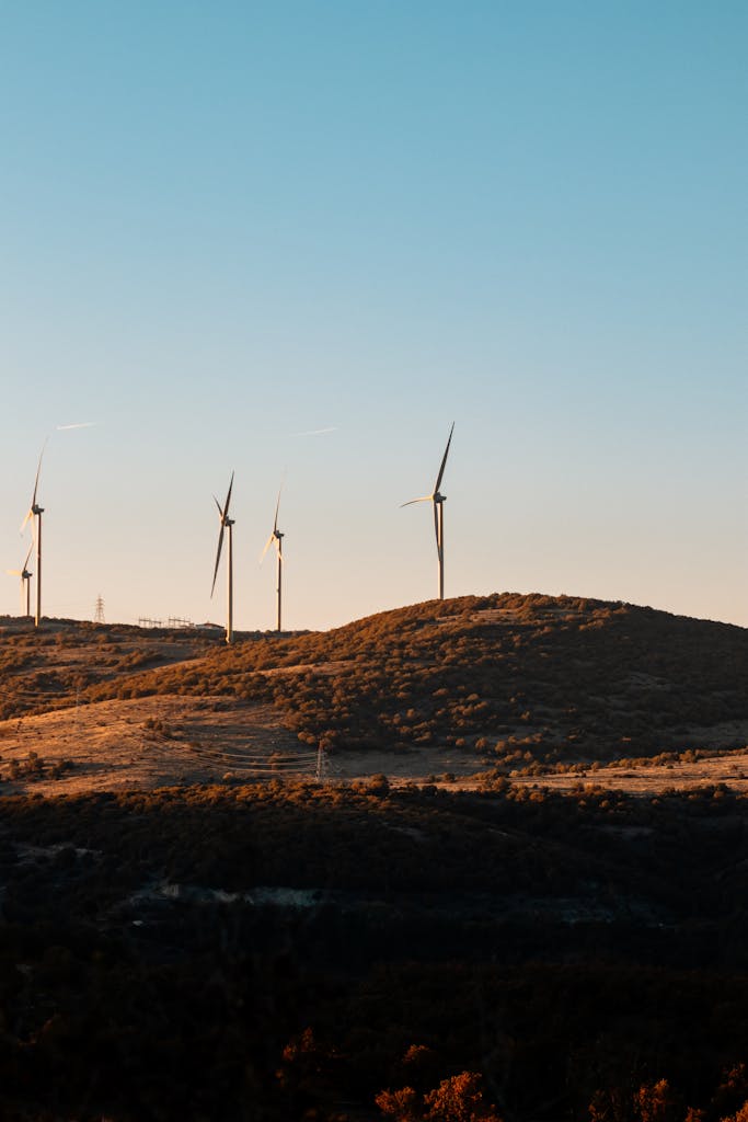 Wind turbines generating renewable energy on a scenic hillside during sunset.